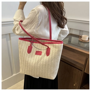 Detail of a large straw tote bag featuring contrast pink leather straps and trim on model