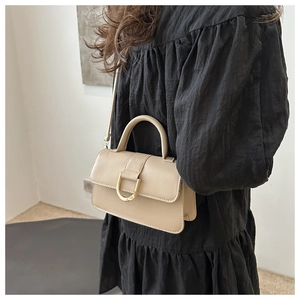 Dettaglio della borsa a tracolla in pelle beige con fibbia a U dorata indossata dal modello
