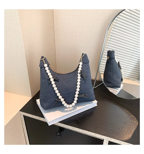 Detail of denim crescent bag featuring a pearl handle and decorative denim bow