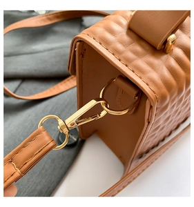 Detail of golden hardware and crocodile embossed texture on a brown leather handbag
