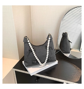 Detail of dark grey tote with pearl chain handles and black velvet bows on a table
