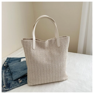 Detail of a beige woven straw tote bag with white leather straps and V-shaped texture
