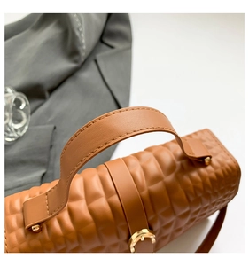 Detailed close-up of brown crocodile embossed leather texture and gold buckle on handbag