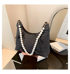 Detail of black denim crescent bag with bow accents and large white pearl handle