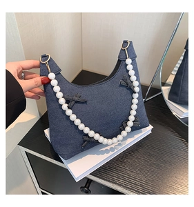 Detail of dark blue denim handbag featuring a chic pearl handle and bow decoration