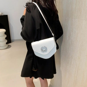Sacoche blanche avec boucle fleur en cristal porté par un mannequin devant un mur