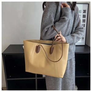 Minimalist cream tote bag with brown straps styled on model in grey knitwear