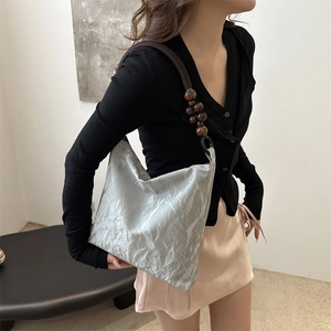 Silver metallic pleated shoulder bag with wooden beaded rope strap on a model