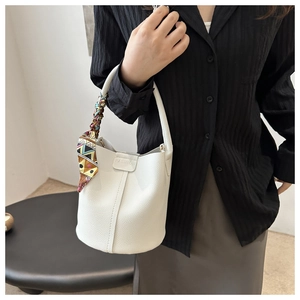 Detail einer weißen Eimer-Tasche aus Leder mit Fashion-Aufdruck und buntem Seidenschal