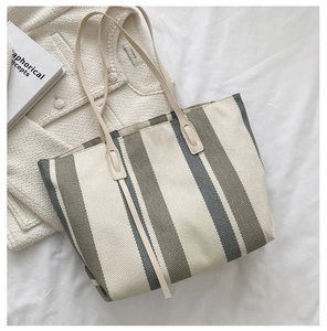 Detail of a large striped canvas tote bag in beige and green on white bedding