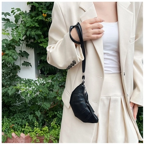 Detailed view of mini black croissant bag with pleated texture worn on beige blazer