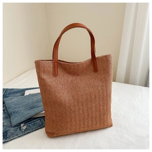Detailed view of woven tote bag with brown leather handles on white textured surface