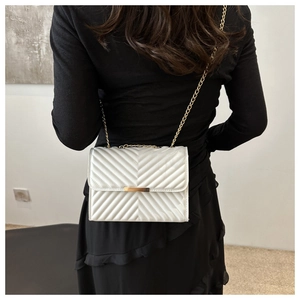 Close-up of white quilted leather flap bag with gold clasp worn over a black dress