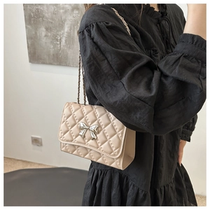 Close-up of beige quilted crossbody bag with silver bow accent and chain strap worn by model