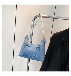 Detailed view of light blue denim hobo bag featuring 3D bows and white pearl strap