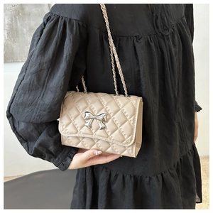 Close-up of beige quilted crossbody bag with silver bow clasp and chain strap