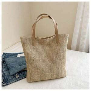 Detail of herringbone weave texture and brown leather handle on a straw tote bag