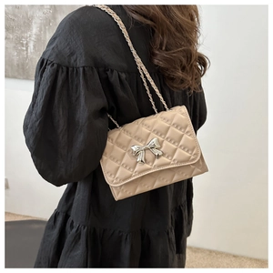 Detail of apricot quilted chain bag with silver bow buckle on black dress