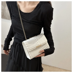 Close-up of white V-quilted chain crossbody bag with gold metal trim on model