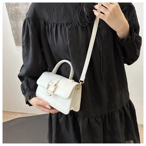 Detail of white faux leather crossbody bag with metal buckle on black dress