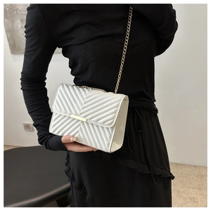 Detail of white V-quilted small flap bag with gold chain strap and metal clasp on a model