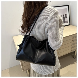 Dettaglio della borsa tote in pelle nera con lettere minimaliste in rilievo e spalline sottili