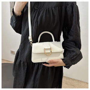 Detail of white mini square crossbody bag with gold buckle on a black dress