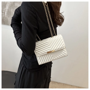 Detail of white quilted leather crossbody bag with elegant gold chain strap on shoulder