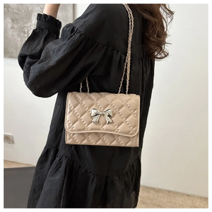 Detail of beige quilted shoulder bag featuring silver metal bow and woven chain strap