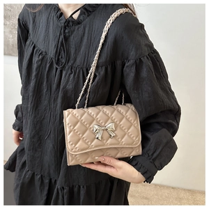 Close-up of beige quilted crossbody bag with silver bow accent and chain strap