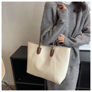 Detail of minimalist cream tote bag with brown straps shown on a model in a studio