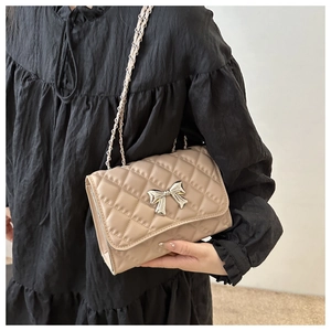 Detail of beige quilted flap bag with silver bow accent and leather chain strap