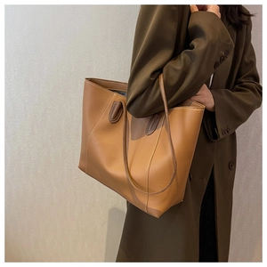Detail of a brown leather tote bag with white contrast stitching on an olive coat