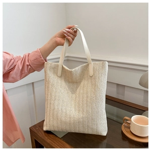 Detail of herringbone woven straw tote bag with cream leather handle on wooden desk