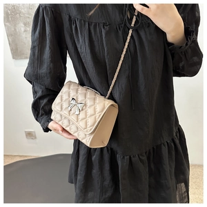 Detail of beige quilted flap bag with silver bow buckle and chain strap on a model