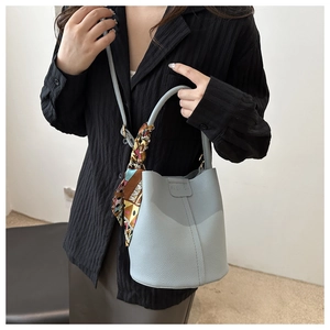 Details der hellblauen Eimer-Tasche aus Leder mit dekorativem Seidenschal und Fashion-Logo