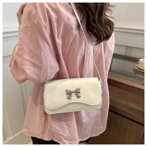 Detail of white square flap crossbody bag featuring a silver metal butterfly buckle accent