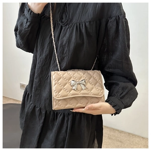 Quilted beige crossbody bag with silver bow buckle worn on a black pleated dress