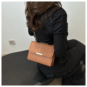Detailed view of caramel brown V-quilted crossbody bag with gold chain strap on model