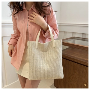 Detail of beige straw tote bag featuring white leather handles and V-shaped woven pattern