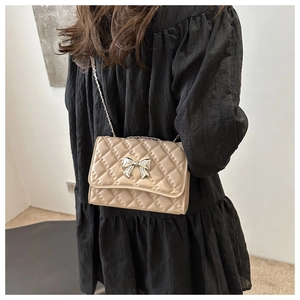 Detail of beige quilted crossbody bag featuring silver bow clasp and chain strap