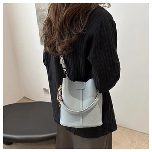 Detailansicht einer hellblauen Eimertasche aus Leder mit Seidenschal und FASHION-Prägung