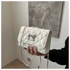Detailed view of white quilted shoulder bag with silver metallic bow and chain strap