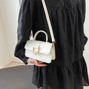 Piccola borsa quadrata bianca in pelle con fibbia dorata su un vestito nero chic