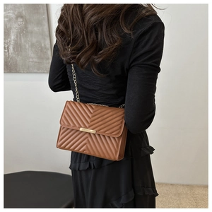 Brown quilted crossbody bag with gold chain strap shown on model in modern interior