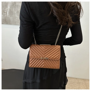 Rear view of brown quilted crossbody bag with gold chain strap on model's shoulder