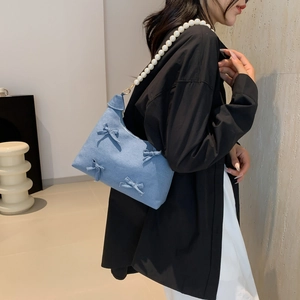 Blue denim underarm bag with bow details and white pearl chain strap on model