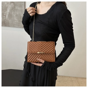 Detail of a brown quilted chain bag with V-shaped stitching and gold metal clasp