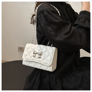 Detail of white quilted crossbody bag featuring a silver metal bow and chain strap