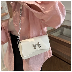 Detailed close-up of a white leather crossbody bag with a silver butterfly bow accent